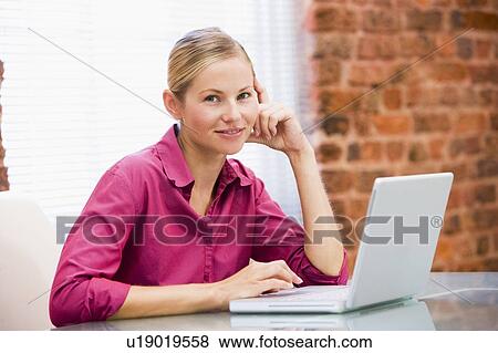 Stock Photo - Businesswoman sitting in office with laptop smiling. Fotosearch