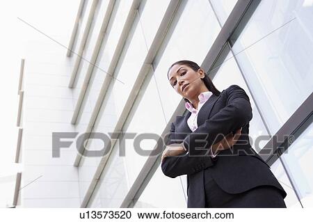 Stock Image - Businesswoman standing outdoors by building (high key/selective focus). Fotosearch