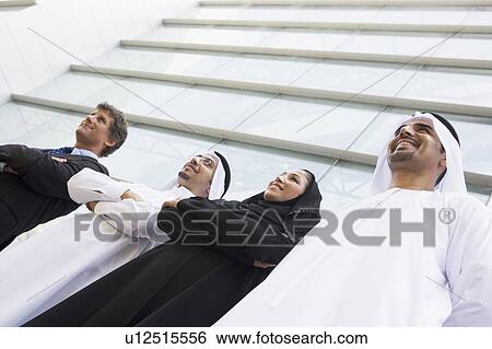 Stock Photograph - Four businesspeople standing outdoors by building smiling (selective focus). Fotosearch