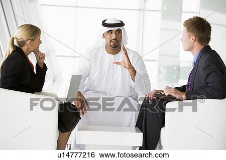Three businesspeople indoors with a laptop talking and smiling (high key/selective focus) View Large Photo Image Stock Photograph - Three businesspeople indoors with a laptop talking and smiling (high key/selective focus). Fotosearch