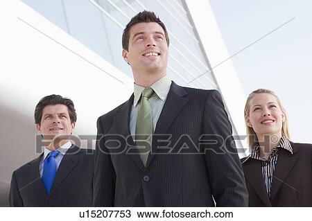 Stock Image - Three businesspeople standing outdoors by building smiling. Fotosearch
