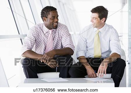 Two businessmen sitting in office lobby talking and smiling View Large Photo Image Stock Photograph - Two businessmen sitting in office lobby talking and smiling. Fotosearch