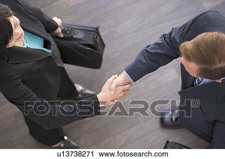 Stock Image - Two businesspeople standing indoors shaking hands. Fotosearch