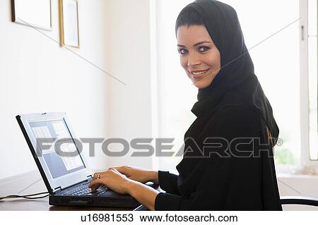 Stock Image - Woman in office with laptop smiling (high key/selective focus). Fotosearch