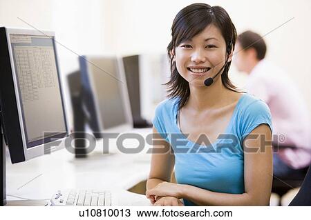 Stock Image - Woman wearing headset in computer room smiling. Fotosearch