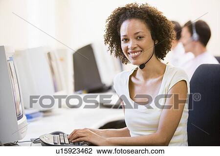 Stock Image - Woman wearing headset in computer room smiling. Fotosearch