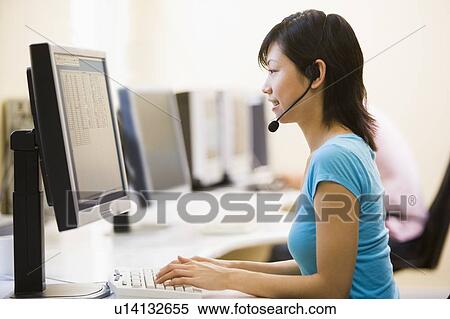 Woman wearing headset in computer room typing and smiling View Large Photo Image Stock Photography - Woman wearing headset in computer room typing and smiling. Fotosearch