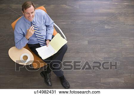 Stock Image - Businessman sitting indoors with coffee and folder smiling. Fotosearch