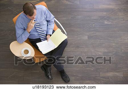 Stock Image - Businessman sitting indoors with coffee and folder. Fotosearch