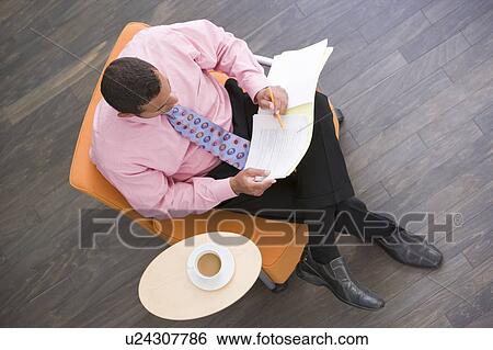 Businessman sitting indoors with coffee and folder View Large Photo Image Stock Photograph - Businessman sitting indoors with coffee and folder. Fotosearch