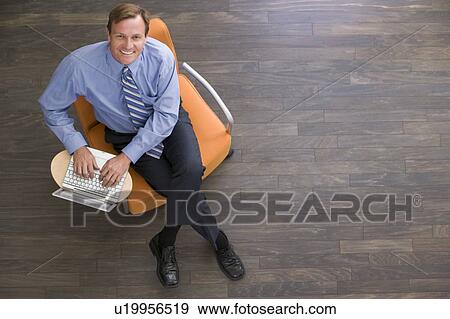 Businessman sitting indoors with laptop smiling View Large Photo Image Stock Photo - Businessman sitting indoors with laptop smiling. Fotosearch