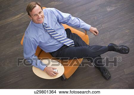 Businessman sitting indoors with cellular phone smiling View Large Photo Image Picture - Businessman sitting indoors with cellular phone smiling. Fotosearch