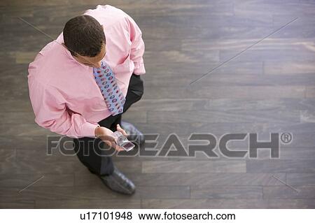 Businessman standing indoors looking at cellular phone View Large Photo Image Stock Photo - Businessman standing indoors looking at cellular phone. Fotosearch