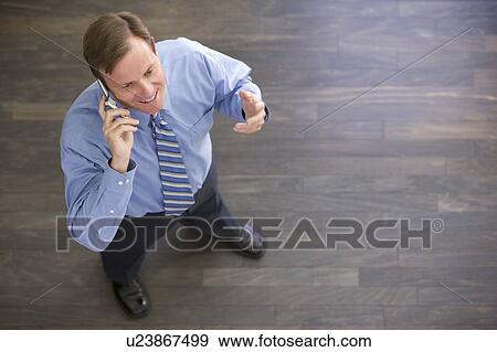 Businessman standing indoors using cellular phone and smiling View Large Photo Image Stock Photo - Businessman standing indoors using cellular phone and smiling. Fotosearch