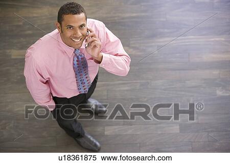 Businessman standing indoors using cellular phone smiling View Large Photo Image Stock Photography - Businessman standing indoors using cellular phone smiling. Fotosearch