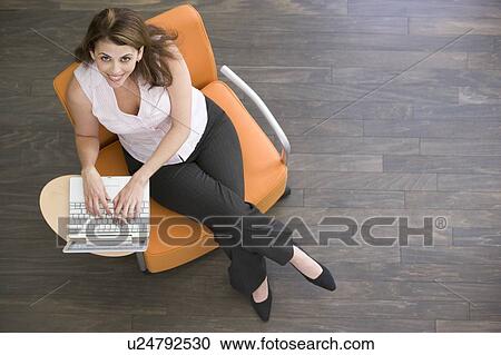 Stock Image - Businesswoman sitting indoors with laptop smiling. Fotosearch