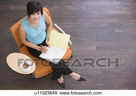 Businesswoman sitting indoors with coffee and folder smiling View Large Photo Image Stock Photo - Businesswoman sitting indoors with coffee and folder smiling. Fotosearch