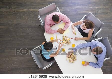 Stock Photo - Four businesspeople at boardroom table with sandwiches. Fotosearch