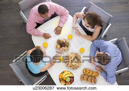 Stock Photo - Four businesspeople at boardroom table with breakfast. Fotosearch