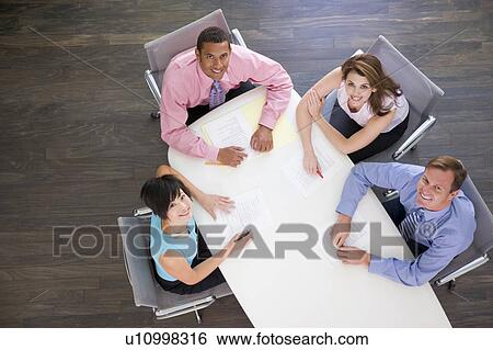 Stock Photograph - Four businesspeople at boardroom table smiling. Fotosearch