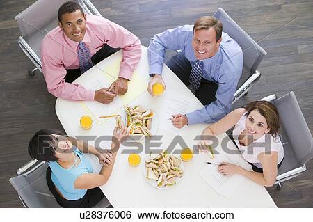 Stock Photograph - Four businesspeople at boardroom table with sandwiches smiling. Fotosearch