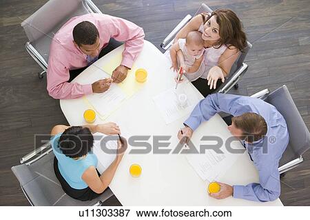 Stock Photo - Four businesspeople in boardroom with one holding a baby smiling. Fotosearch