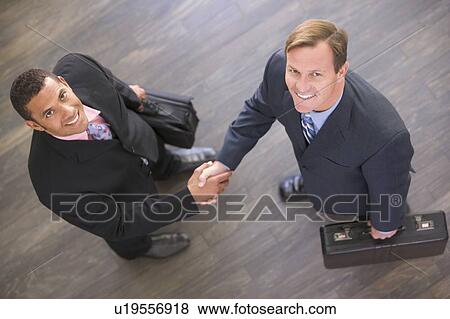 Stock Photo - Two businessmen indoors shaking hands smiling. Fotosearch