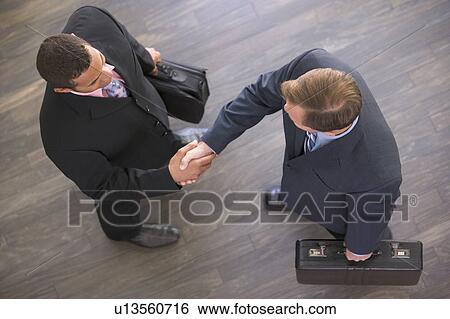 Stock Photograph - Two businessmen indoors shaking hands. Fotosearch