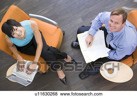 Stock Photo - Two businesspeople sitting indoors with coffee laptop and folder smiling. Fotosearch