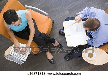 Stock Photo - Two businesspeople sitting indoors with coffee laptop and folder. Fotosearch