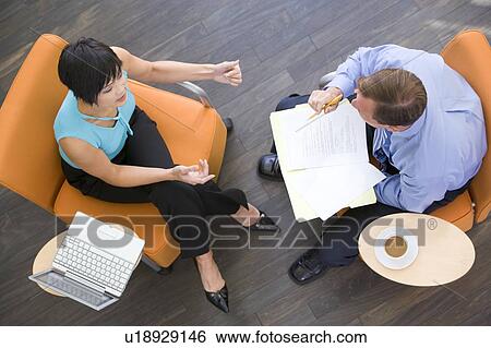 Stock Photograph - Two businesspeople sitting indoors with coffee laptop and folder. Fotosearch