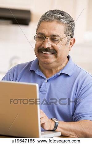 Stock Photography - Man in kitchen with laptop smiling. Fotosearch