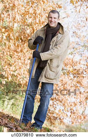 Stock Image - Man outdoors raking leaves and smiling (selective focus). Fotosearch
