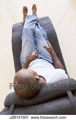 Stock Image - Man sitting in chair listening to MP3 player. Fotosearch
