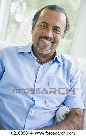 Man sitting in living room smiling (high key/selective focus) View Large Photo Image Picture - Man sitting in living room smiling (high key/selective focus). Fotosearch