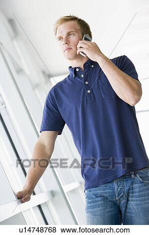 Stock Photo - Man standing in corridor smiling using cellular phone. Fotosearch