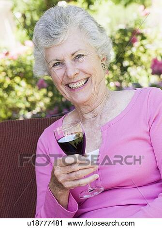 Senior woman sitting outdoors on a chair with a glass of red wine View Large Photo Image Stock Image - Senior woman sitting outdoors on a chair with a glass of red wine. Fotosearch