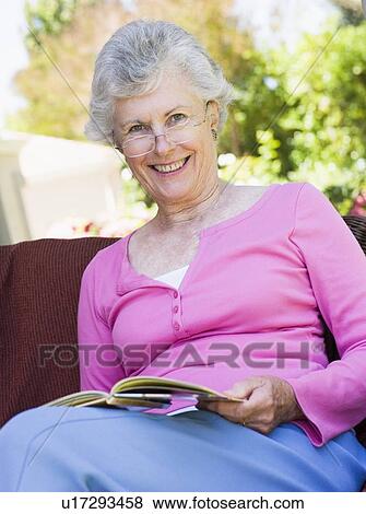 Senior woman sitting outdoors on a chair reading a book View Large Photo Image Stock Photo - Senior woman sitting outdoors on a chair reading a book. Fotosearch