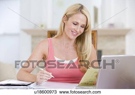 Stock Image - Woman in dining room with laptop smiling. Fotosearch