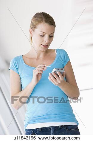 Woman standing in corridor using personal digital assistant View Large Photo Image Stock Photograph - Woman standing in corridor using personal digital assistant. Fotosearch