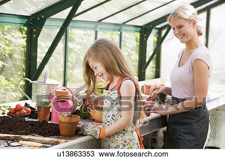 Stock Image - Young girl and woman in greenhouse putting soil in pots smiling. Fotosearch