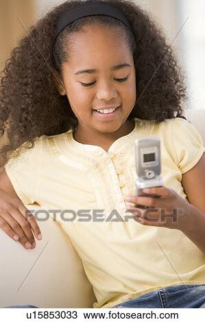Stock Image - Young girl in living room using cellular phone and smiling. Fotosearch