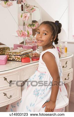 Stock Image - Young girl sitting at mirror in bedroom smiling. Fotosearch