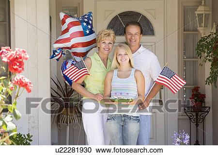 Stock Image - Family at front door on fourth of July with flags and cookies smiling. Fotosearch