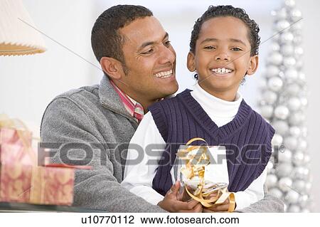Stock Image - Father And Son Hugging, Holding Christmas Gift. Fotosearch