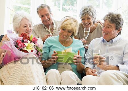 Stock Photograph - Five friends with champagne and gifts in living room smiling. Fotosearch