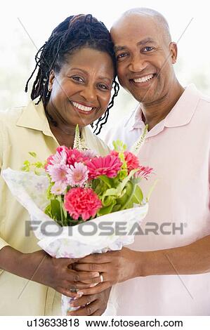 Stock Photo - Husband and wife holding flowers smiling. Fotosearch