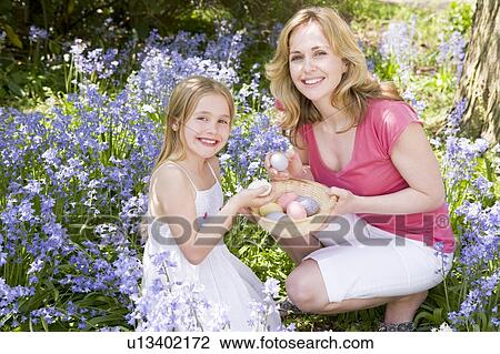 Stock Image - Mother and daughter on Easter looking for eggs outdoors smiling. Fotosearch