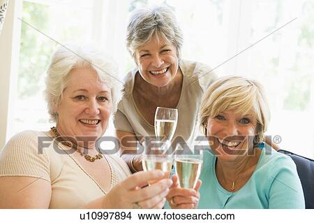 Picture - Three women in living room drinking champagne and smiling. Fotosearch