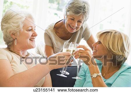 Stock Image - Three women in living room toasting champagne and smiling. Fotosearch